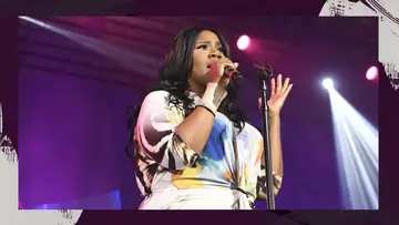 Kelly Price singing in a multi-colored dress, against a purple background.