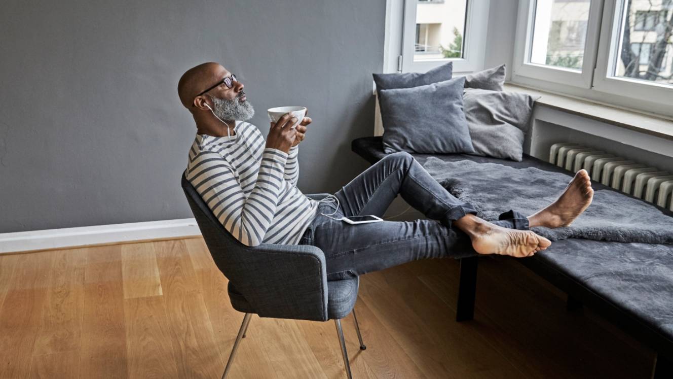 Matureman with earphones sitting at window, drinking coffee - stock photo
