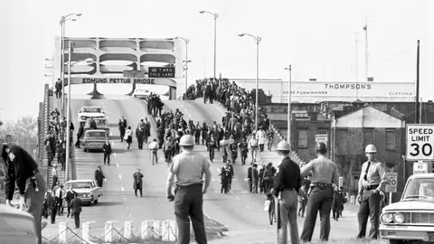 State troopers watch as marchers cross the Edmund Pettus Bridge over the Alabama River in Selma, Alabama as part of a civil rights march on March 9. Two days before troopers used excessive force driving marchers back across the bridge, killing one protester.
