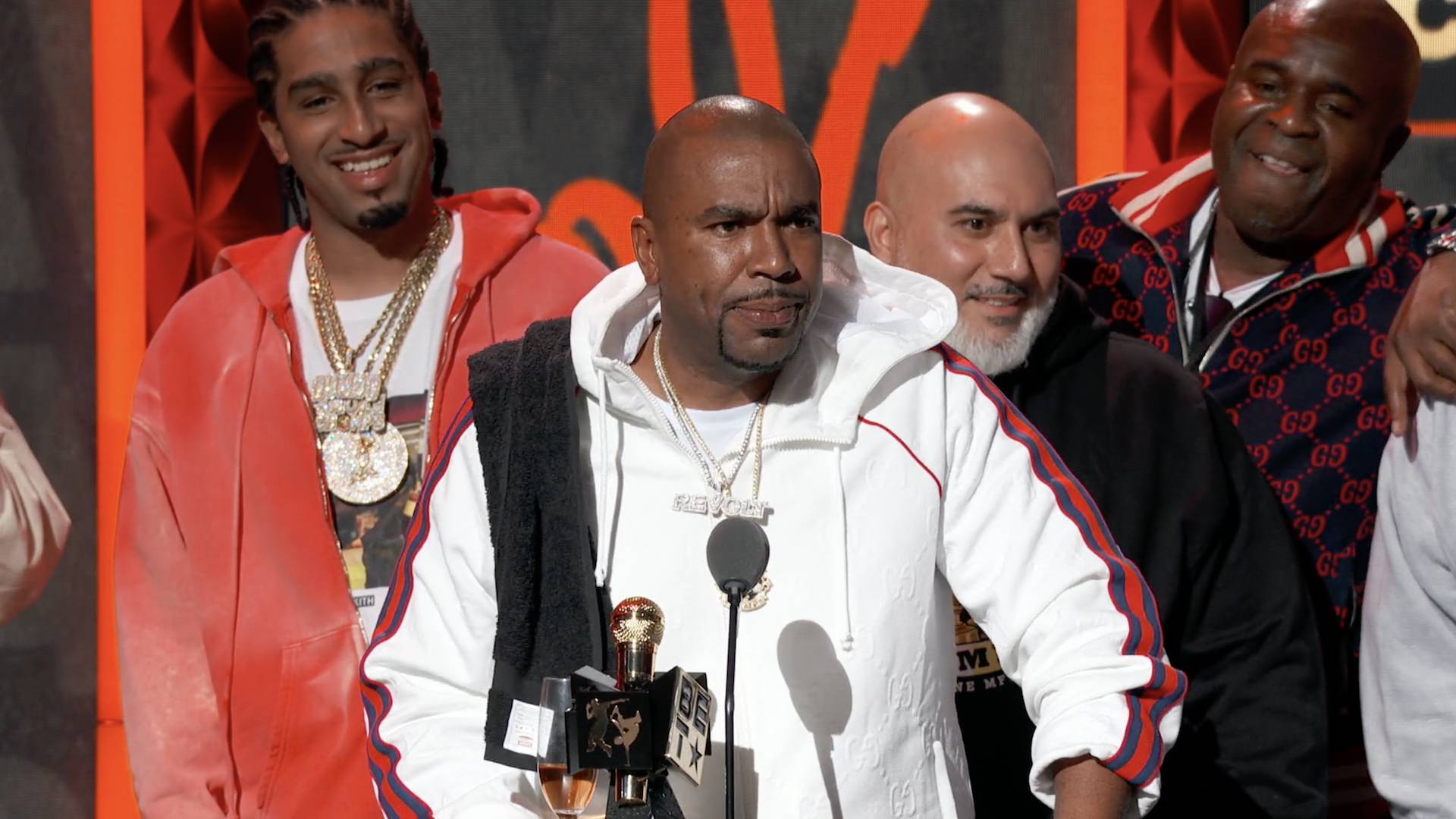 Rapper N.O.R.E. accepting an award in a white hoodie, on stage at the BET Hip Hop Awards 2022.