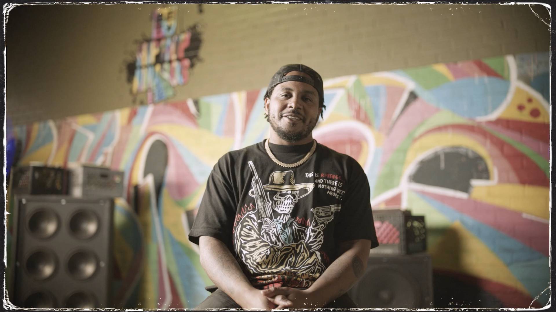 Rapper GRIP in a black shirt and hat, standing in front of a colorful wall.