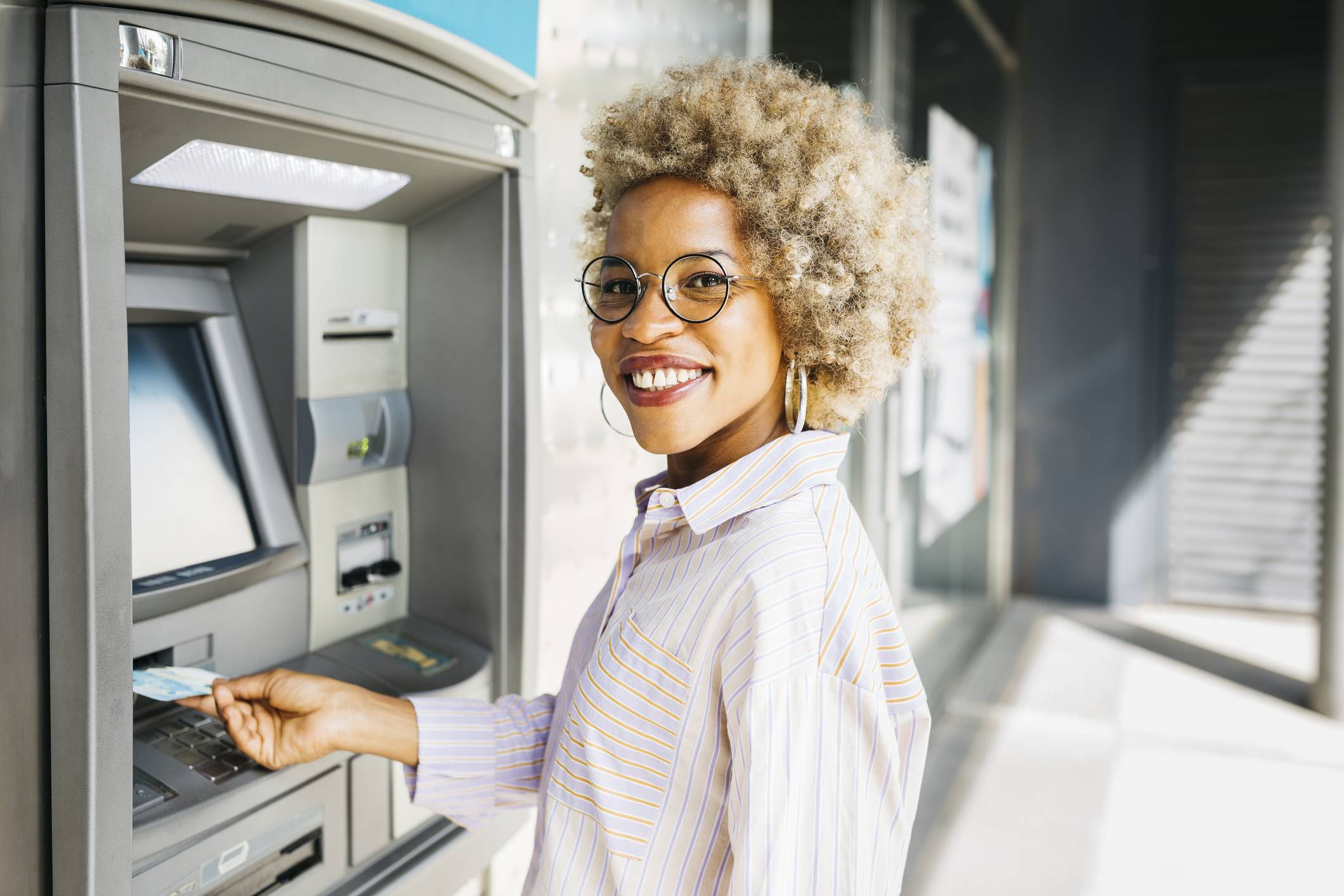 Afro-Latina woman with afro hair, withdrawing money from the ATM.
