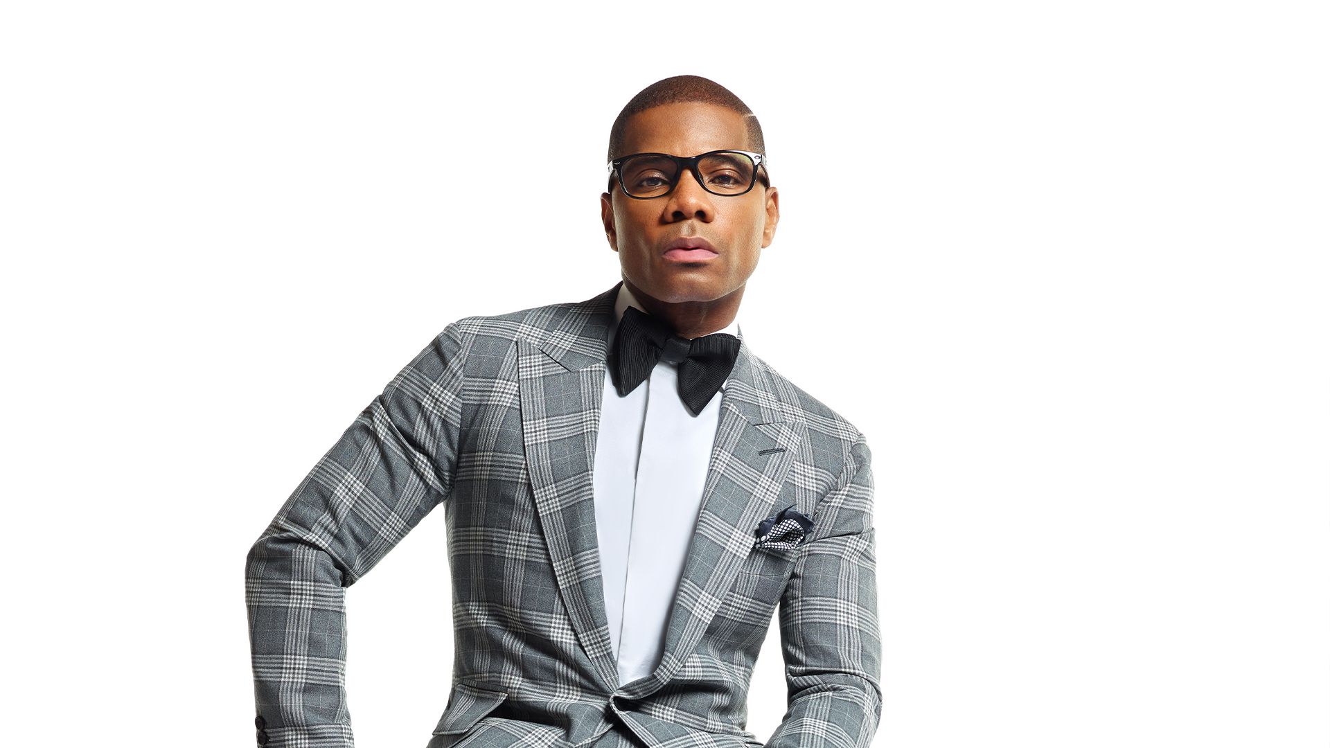Kirk Franklin posing in a grey suit, white shirt, and black bowtie against a white background.
