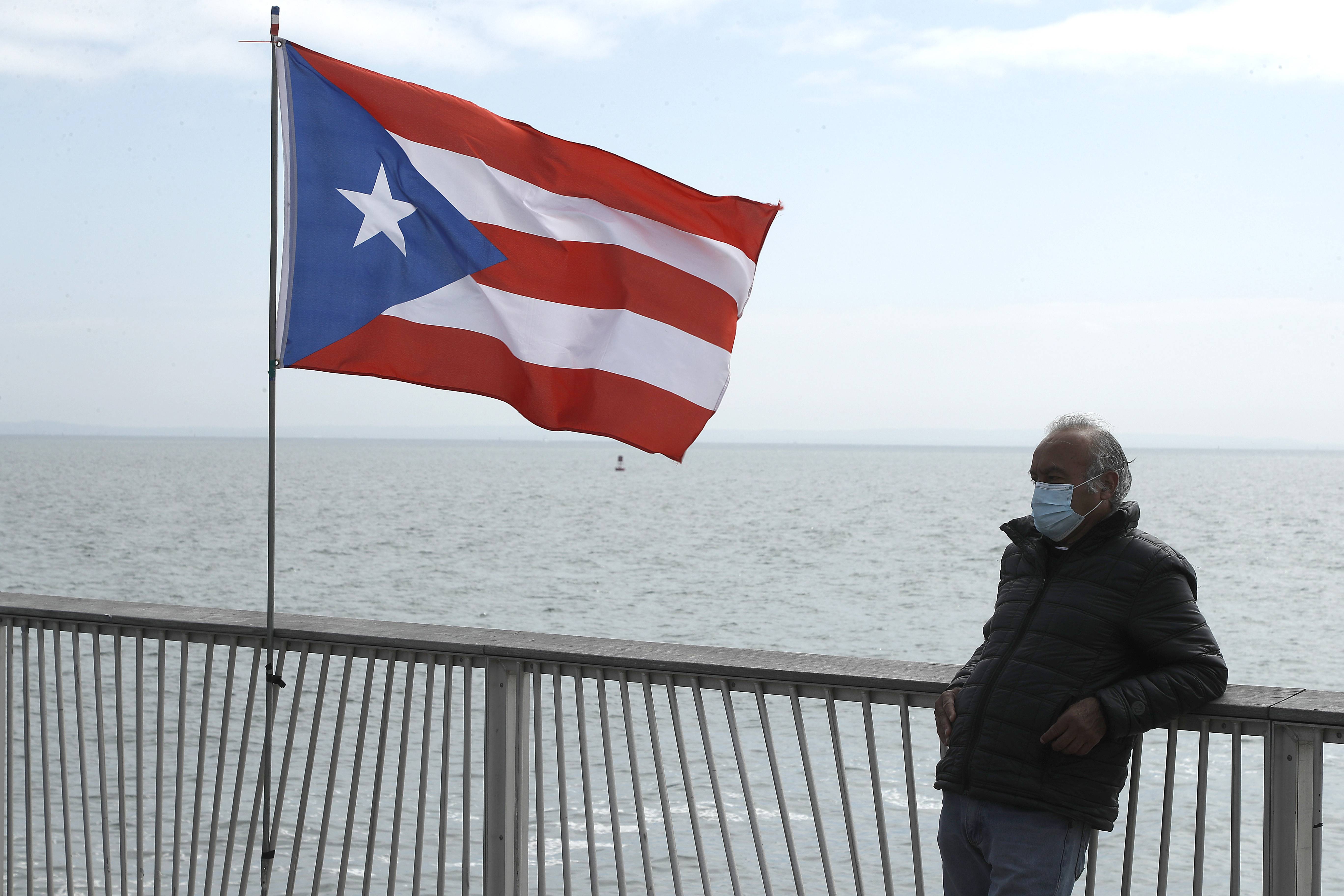 NEW YORK, NEW YORK - MAY 25: A man waring a protective mask stands next to a Puerto Rican flag on Coney Island pier during the coronavirus pandemic on May 25, 2020 in Brooklyn Borough of New York City. Government guidelines encourage wearing a mask in public with strong social distancing in effect as all 50 states in the USA have begun a gradual process to slowly reopen after weeks of stay-at-home measures to slow the spread of COVID-19. (Photo by John Lamparski/Getty Images)