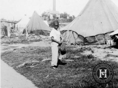 The Displaced - Although the Black community began to rebuild after the Tulsa race massacre, according to the Oklahoma Historical Society, thousands of people were forced to live in tents during the winter of 1921-22. Here. a young African American boy standing near three tents that the American Red Cross erected for the displaced.