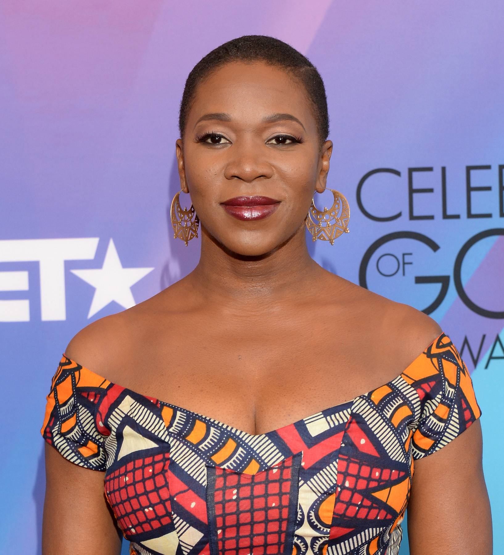 India Arie on a red carpet, wearing a patterned off the shoulder dress