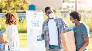 A father and son spend time together sorting food for the community food drive during COVID-19.  They wear protective masks and gloves.