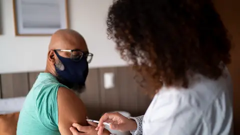 Home call nurse or doctor vaccinating a man at home - wearing face mask