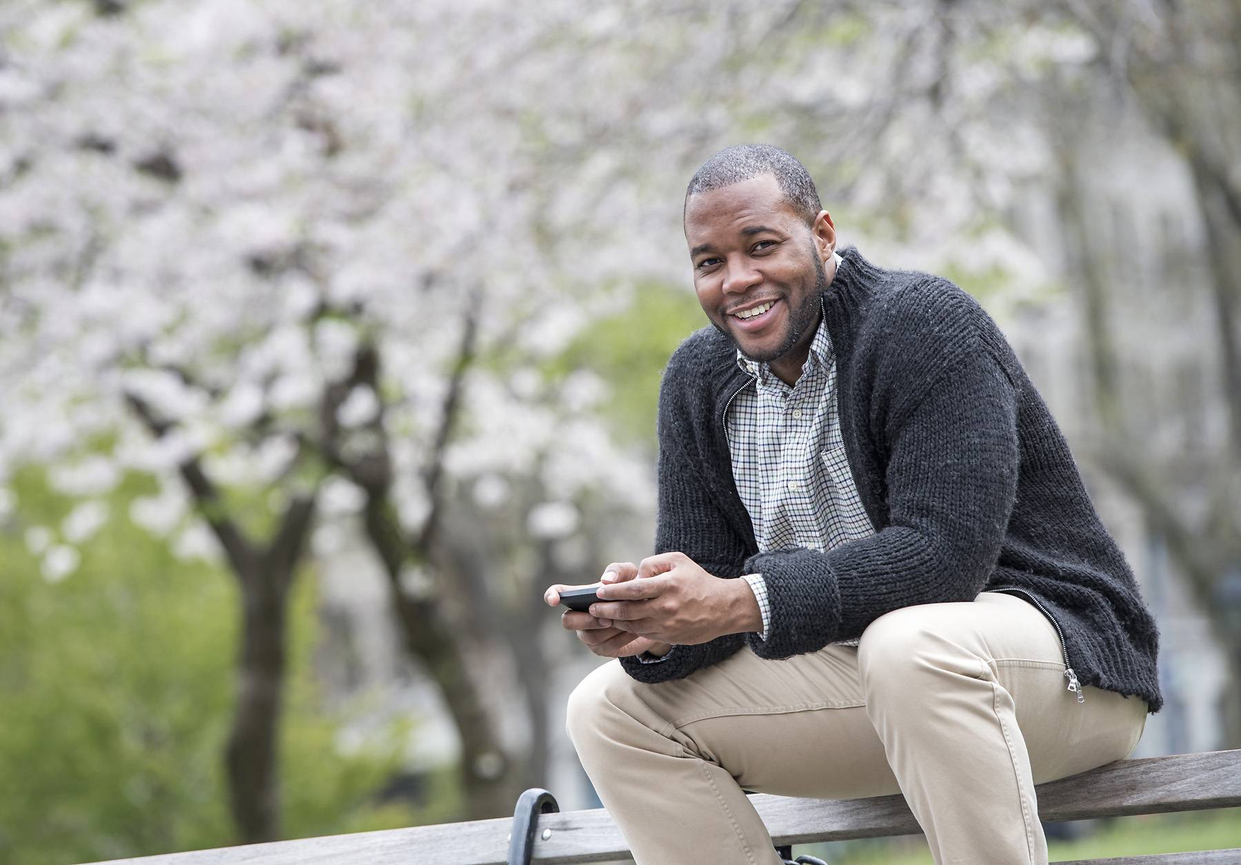 A man sitting on a bench in the park, holding a phone