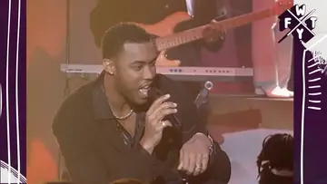 Montell Jordan performing in a black jacket and shirt on stage.