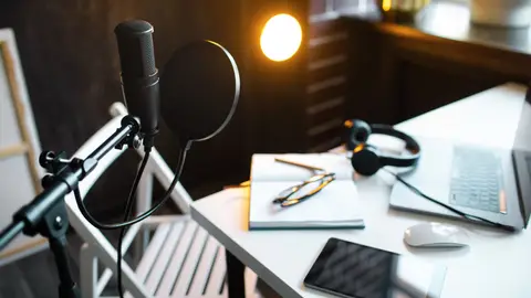 Podcast streaming at home. Audio studio with laptop, microphone with pop filter and headphones on white table against black wall with warm lights. Blogger concept.