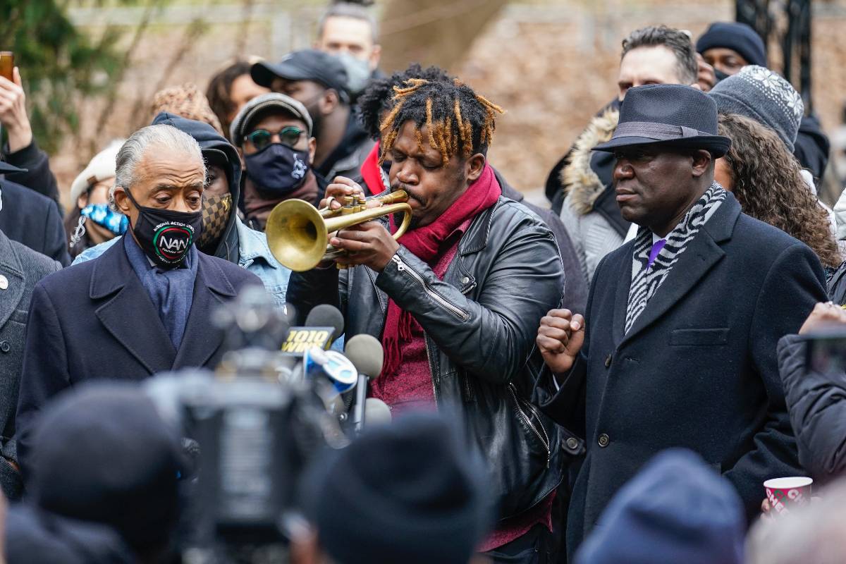 Keyon Harrold Sr. plays the trumpet as Attorney Ben Crump, right, Reverend Al Sharpton, left, listen during a news conference Wednesday, Dec. 30, 2020, in New York. New York City prosecutors say they are investigating a confrontation in which a man said a woman tackled his 14-year-old son in a New York City hotel lobby as she falsely accused the Black teen of stealing her phone. Harrold posted a widely viewed video of the confrontation Saturday at the Arlo Hotel, which prompted comparisons to recent incidents involving false accusations against Black people.  (AP Photo/Frank Franklin II)