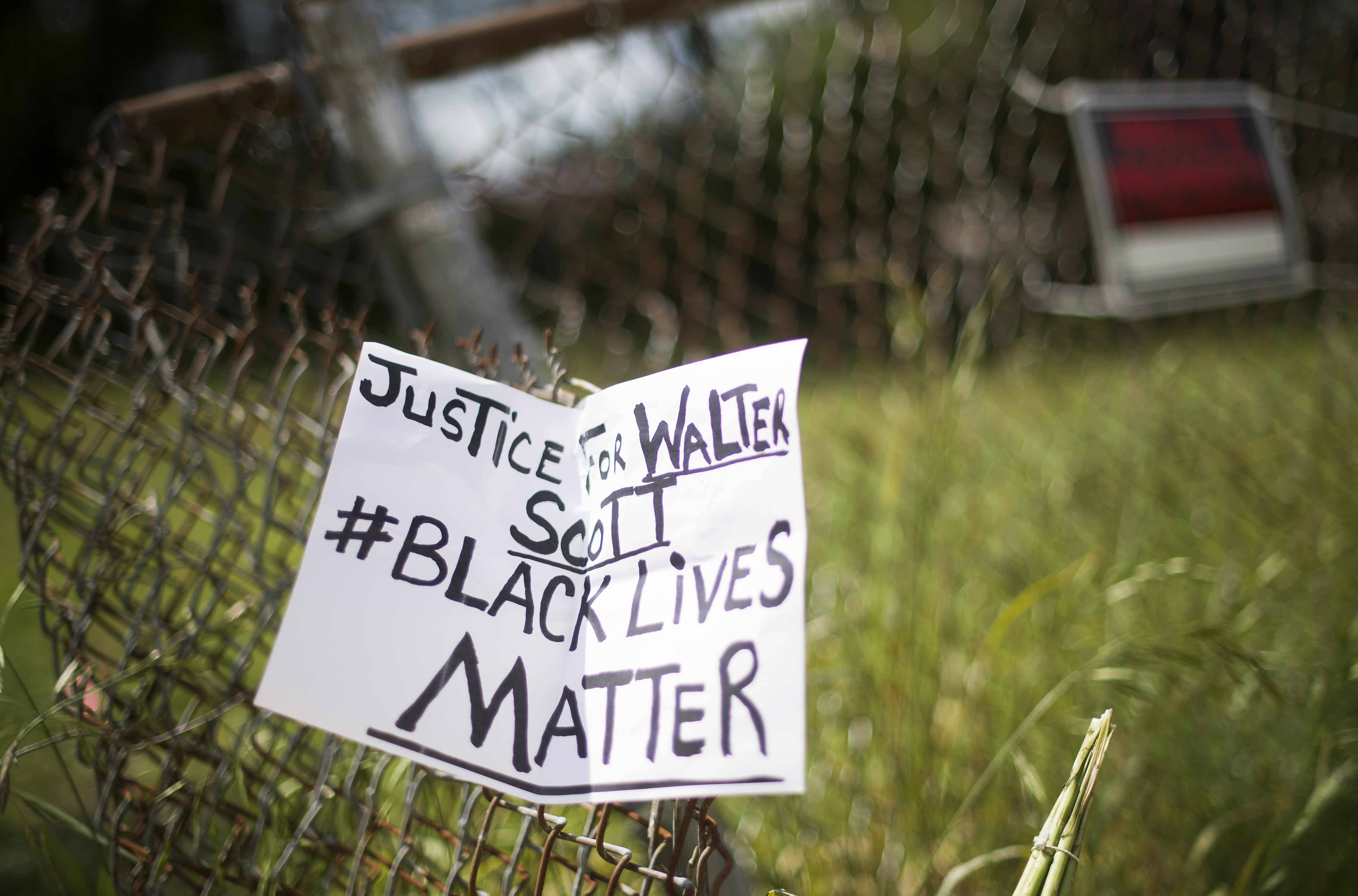 A placard is tied to a fence outside the vacant lot where Walter Scott, the 50-year-old man who was fired at eight times was killed as he ran away from an officer after a traffic stop in North Charleston, South Carolina on April 8, 2015. Police officer Michael Slager,33, who fatally shot Scott in the US city of North Charleston has been fired after he was charged with murder, the mayor said. Speaking at a highly charged press conference frequently interrupted by residents angered at America's latest high-profile police killing of a black man, Mayor Keith Summey said the city had moved quickly to fire the officer after Saturday's shooting.   AFP PHOTO/JIM WATSON        (Photo credit should read JIM WATSON/AFP via Getty Images)