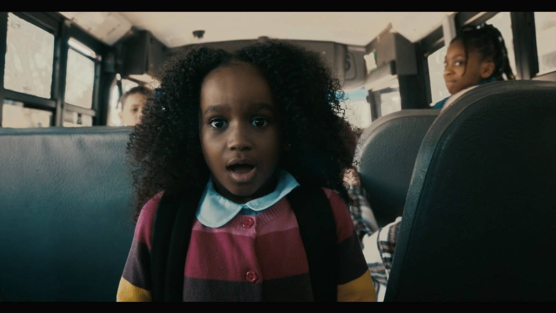 A young girl in a sweater looks surprised on her school bus.