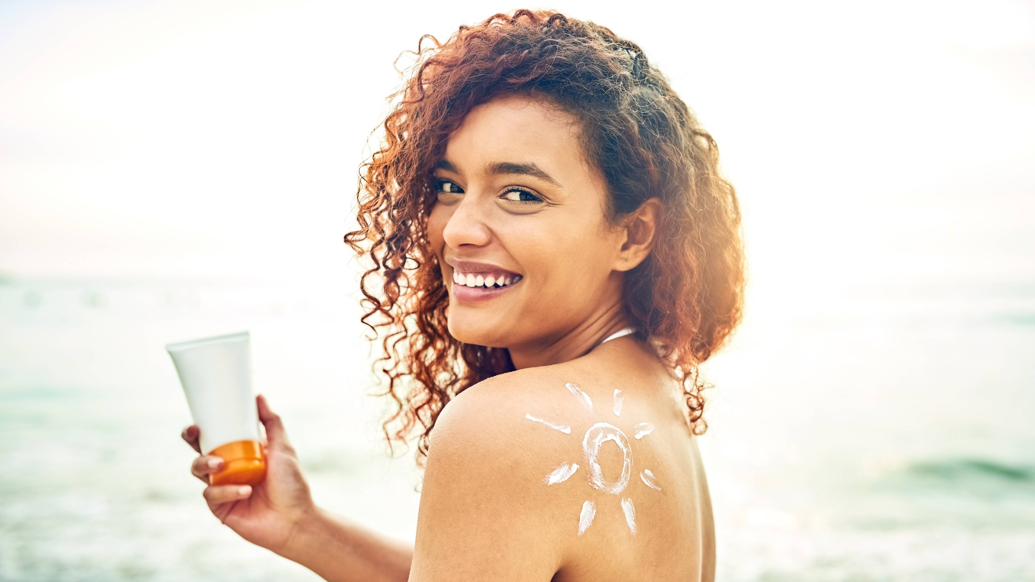 Portrait of a young woman applying sunscreen at the beach