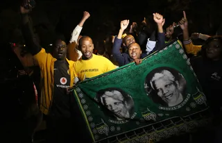 Johannesburg Remembers - South Africans pay tribute to Mandela by holding pictures of the late former president in Johannesburg on Dec. 5.&nbsp; (Photo: ALEXANDER JOE/AFP/Getty Images)