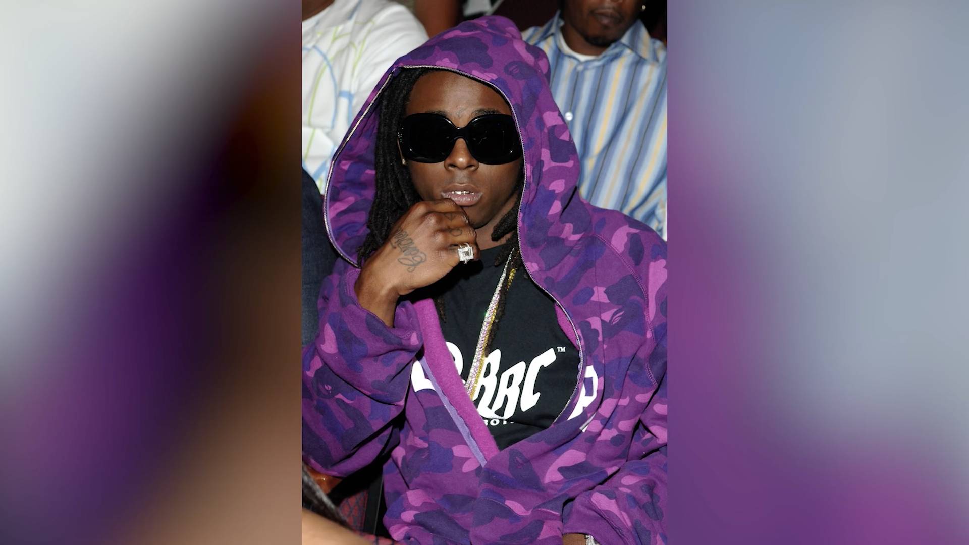 Rapper Lil Wayne in a purple hoodie, black shirt and sunglasses.