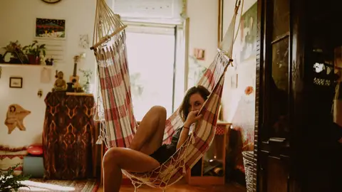 Girl casually lying in plaid coloured hammock in the middle of a ramshackle apartment, looking to the camera