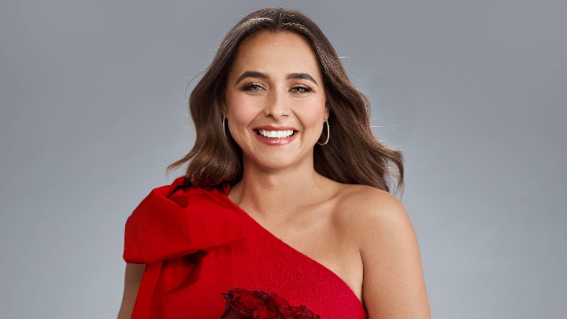 Brooke Blurton smiling in a red dress in front of a grey background