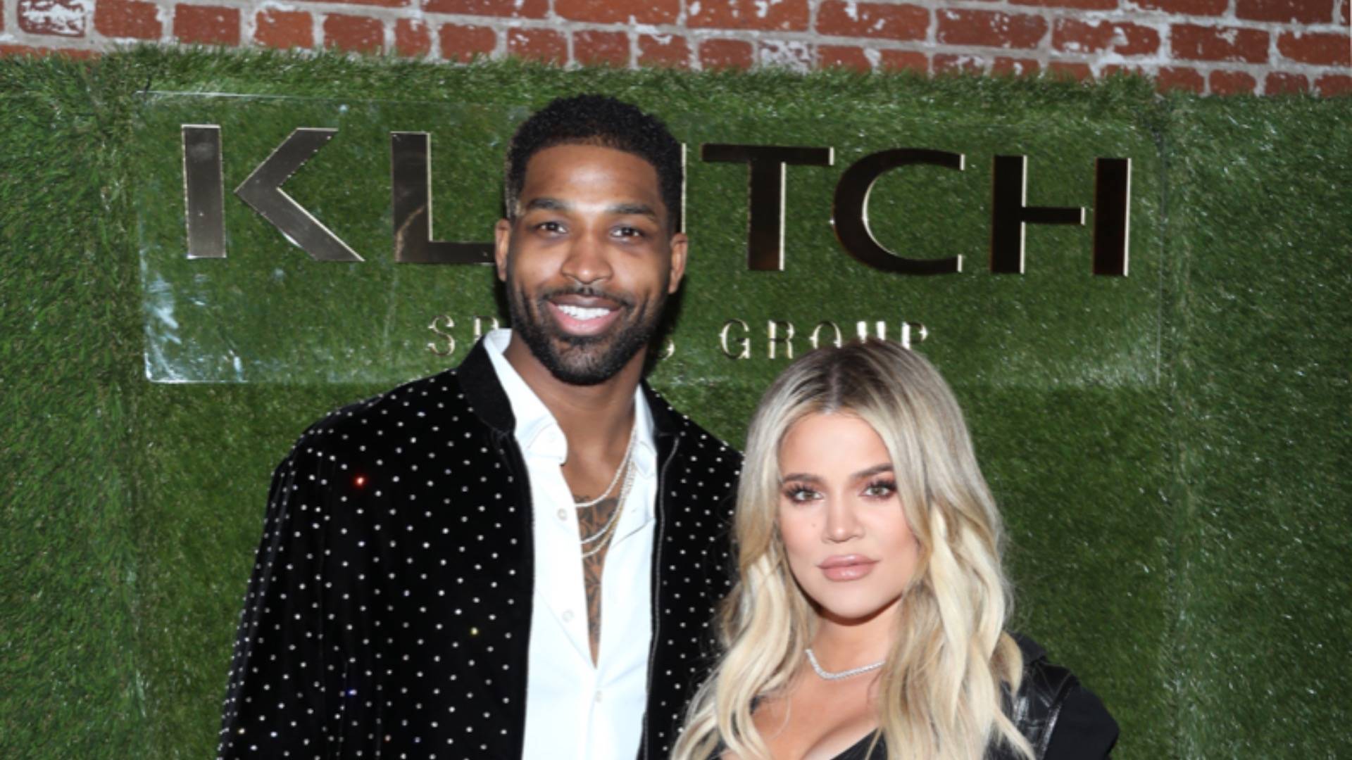Khloe Kardashian and Tristan Thompson posing in front of synthetic green grass background