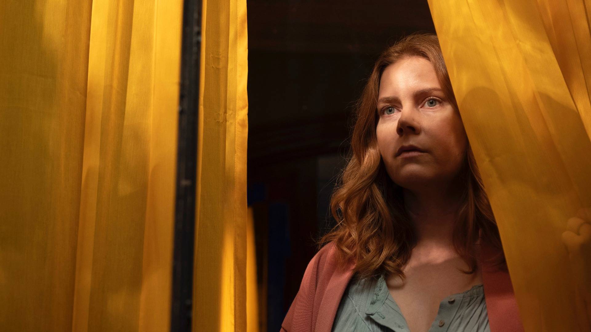 Amy Adams peering out through yellow curtains in Netflix movie 'The Woman In The Window' 