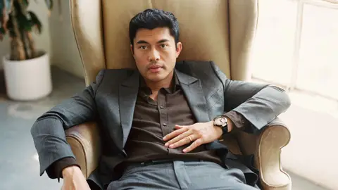 Henry Golding on chair in suit and watch staring for GQ profile 2018