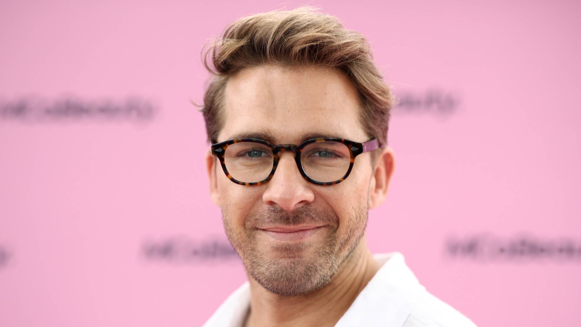 Australian actor Hugh Sheridan wearing plastic glasses and posing in front of pink background