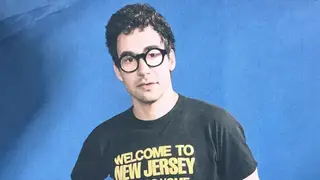 Jack Antonoff poses in front of blue screen in black and yellow shirt welcome to new jersey 