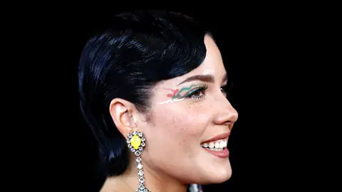 Close-up of Halsey's face smiling with large yellow stone and diamonte earrings and eye art 