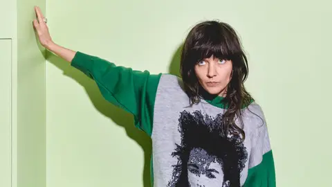 Courtney Barnett in green and grey jumper in front of green wall with fringe