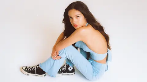 Olivia Rodrigo in black converse high tops blue top and matching blue trousers posing with shoulders out and hair out long