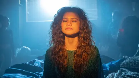 Zendaya with eyes closed on bed blue starring in Euphoria in green jumper 