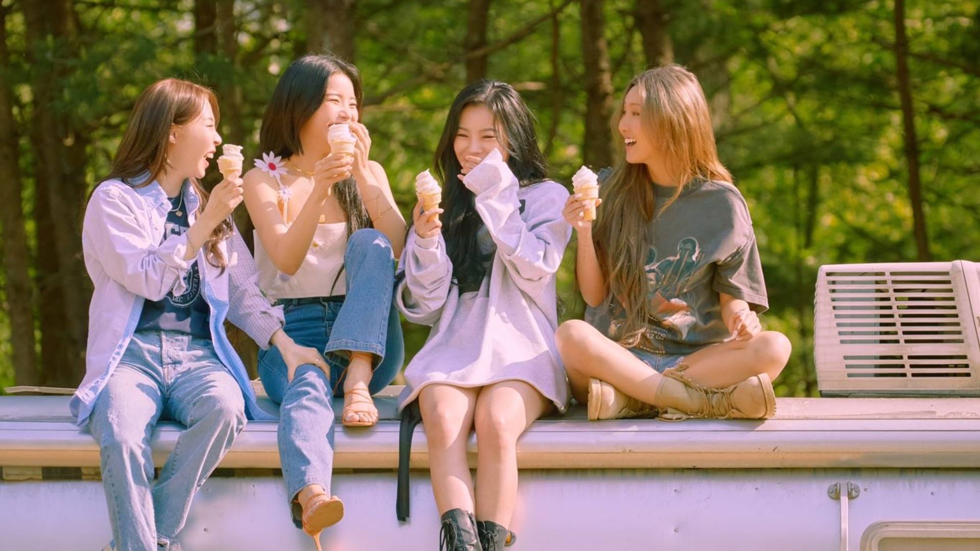 The four members of Korean girl band Mamamoo sitting on top of a truck laughing and eating ice cream cones together 