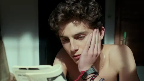 Timothee Chalamet in Call Me By Your Name staring and reading book with watch in 80s 