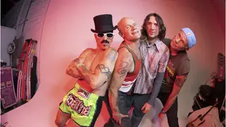 The Red Hot Chili Peppers pose in front of a pink background, with singer Anthony Kiedis shirtless (as always) and in a Willy Wonka-esque top hot.