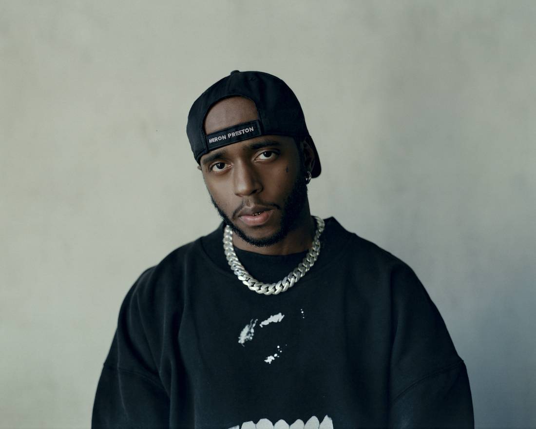 A portrait of the singer/rapper 6lack decked out in black clothes and a black snapback hat