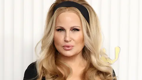 Jennifer Coolidge poses in front of a white background with a black headband