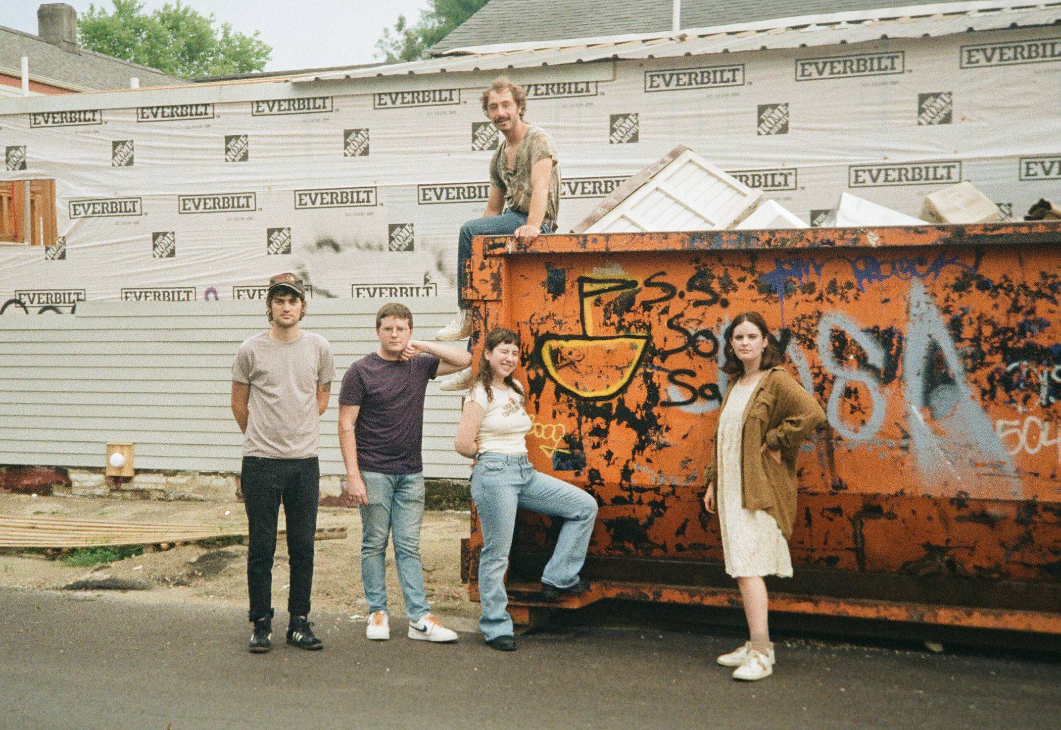Wednesday pose in front of a graffiti'd dumpster