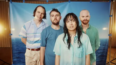 Australian guitar pop band The Beths pose in front of a watery backdrop with wet hair and in beachy clothes.
