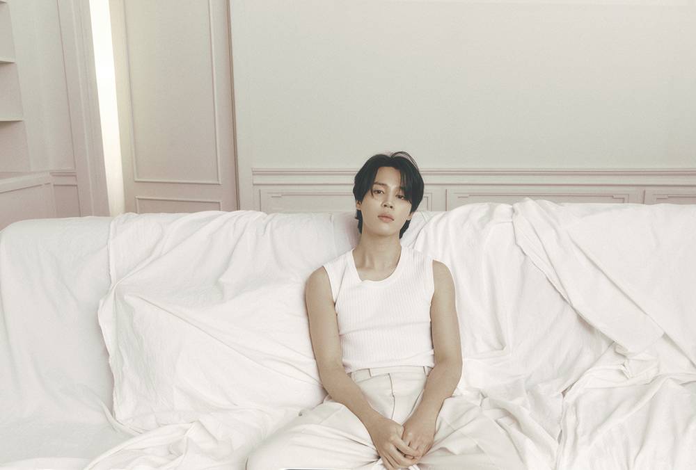 Jimin poses in white on an all-white sofa with white walls behind him