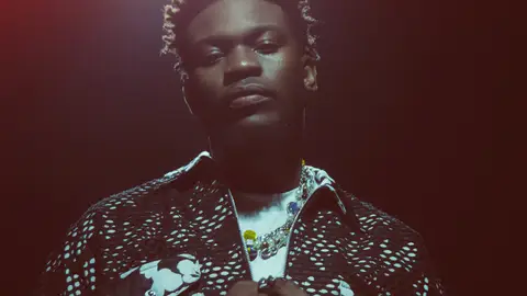 Nonso Amadi poses against a black backdrop, cupping his hands and lit from above