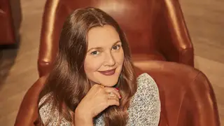 Drew Barrymore poses with an arm under her chin while sitting in a leather armchair