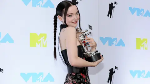 Dove Cameron poses in front of a VMA background with her Moon Person trophy.