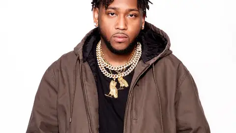 A photo of producer Boi-1da posing in gold chains against a white background