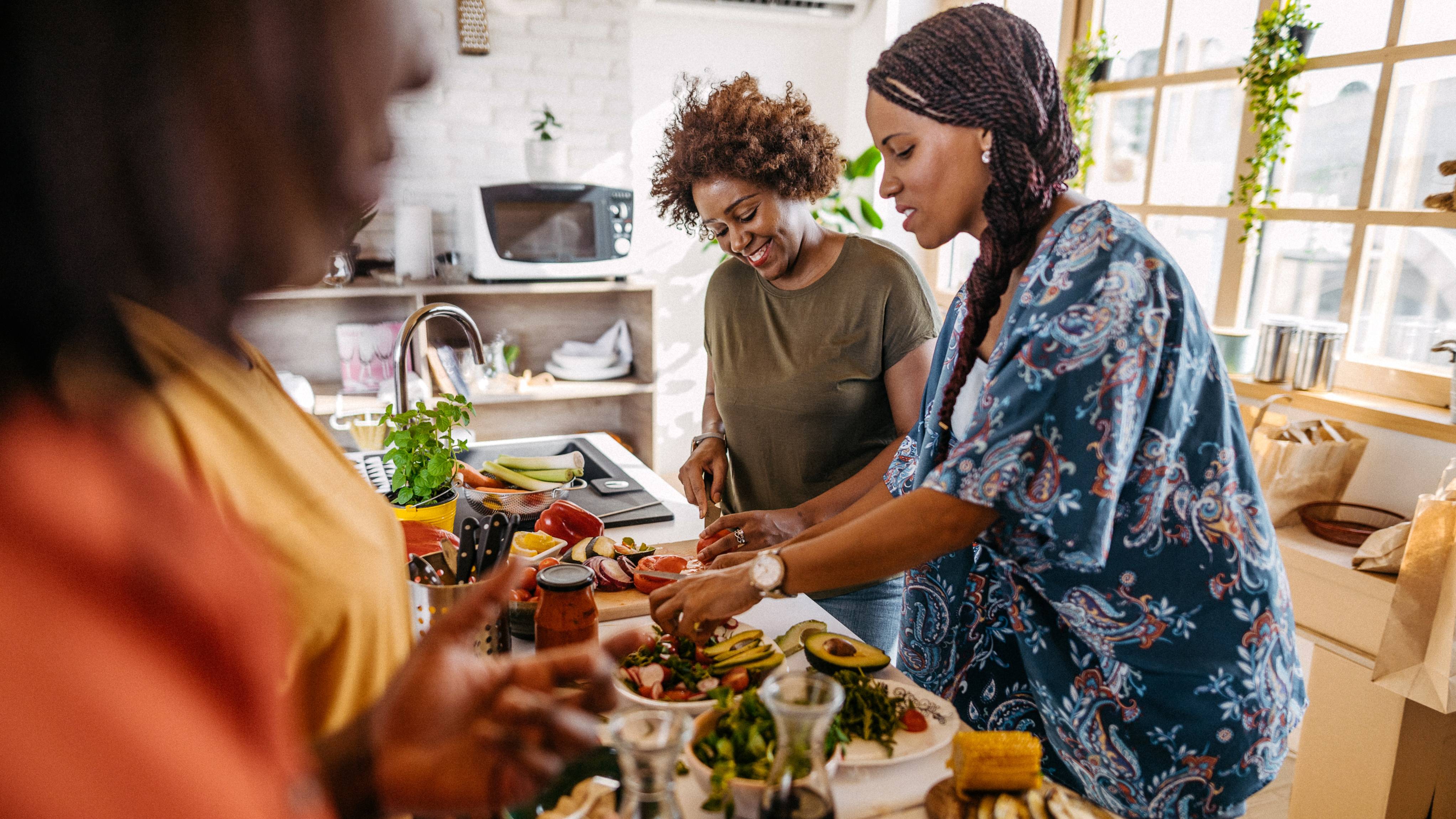 Group of female friends making lunch and talking in the kitchen at apartment