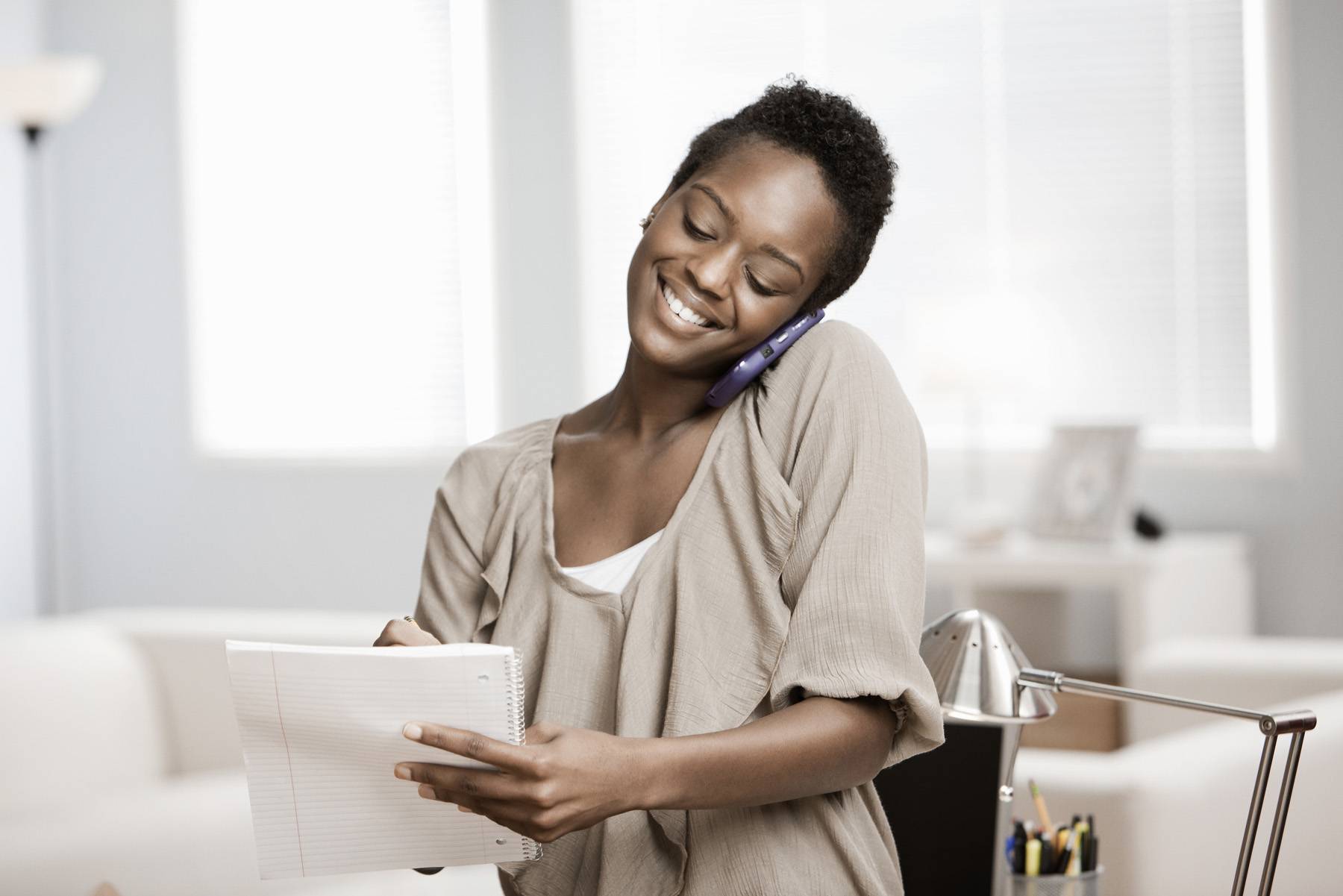 African American woman writing and talking on cellphone