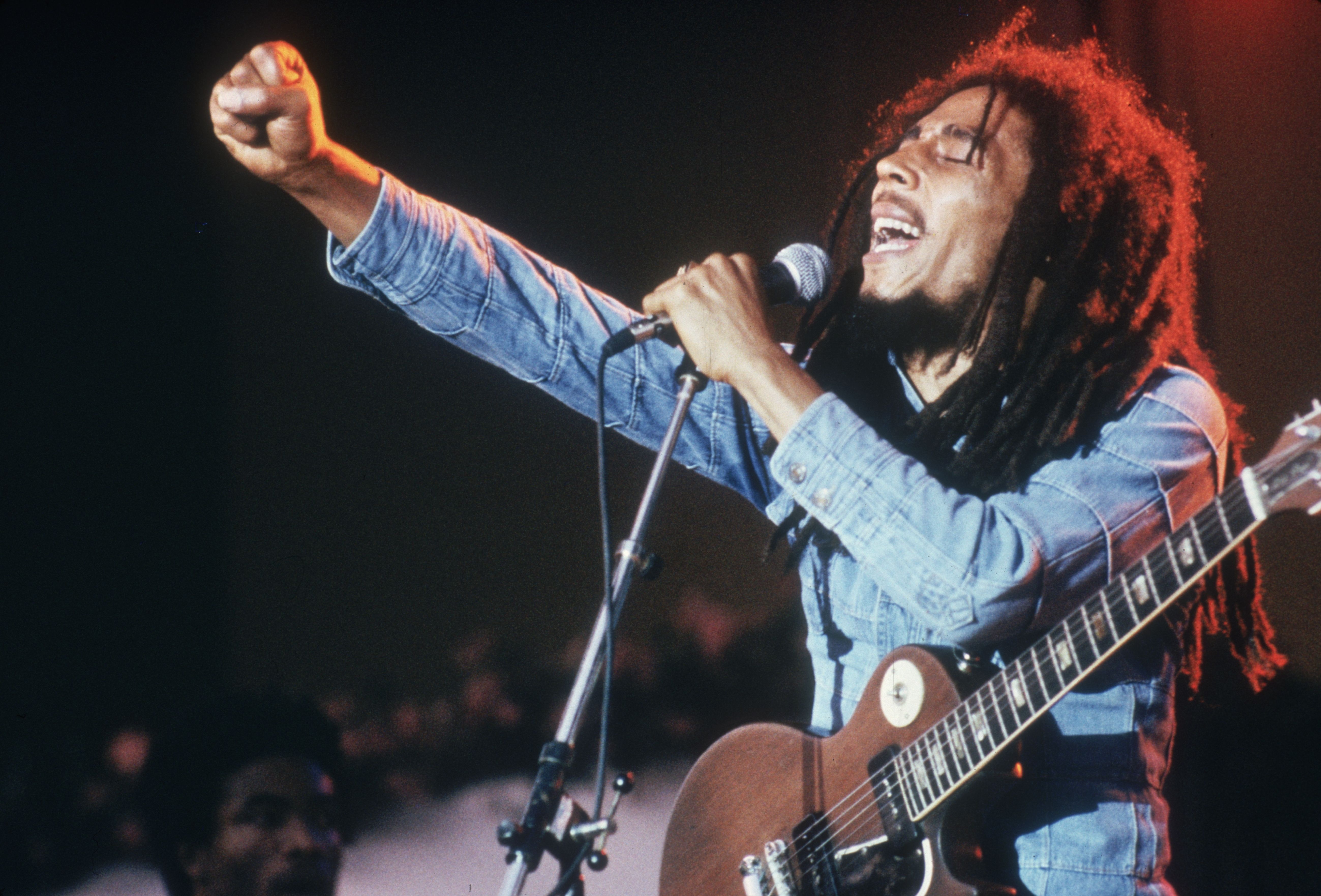 Bob Marley performs on stage, in a concert at Grona Lund, Stockholm, Sweden. He extends his fist as he sings into the microphone, with an electric guitar. (Photo by Hulton Archive/Getty Images)