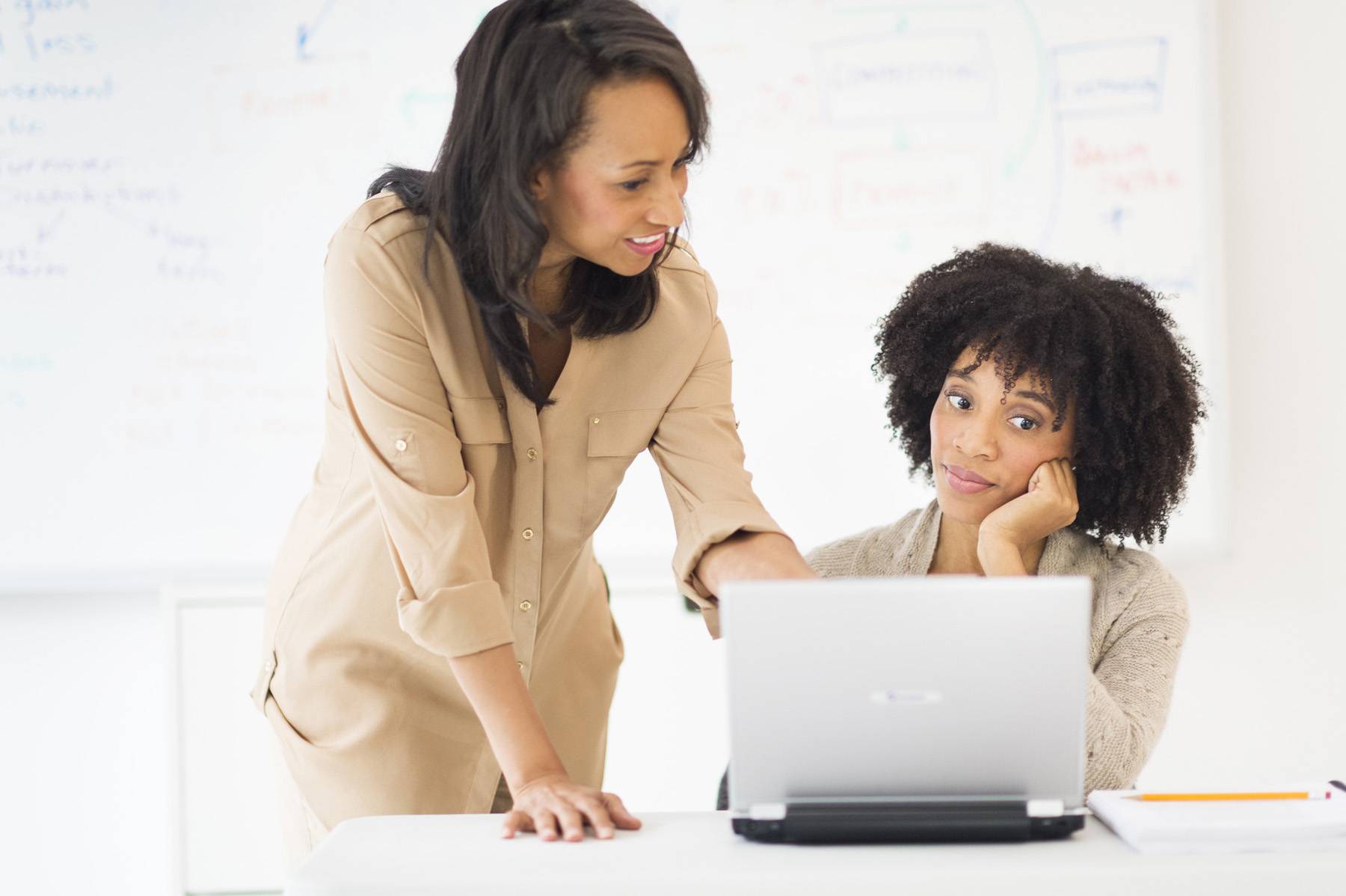 woman teaching female co-worker on laptop