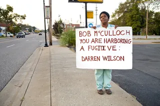 Arrest Overdue - A woman protests on South Florissant outside of the Ferguson Police Department with a sign directed to St. Louis prosecutor&nbsp;Bob McCulloch.&nbsp;(Photo: Lucas Alvarado-Farrar/Whose Streets Media)