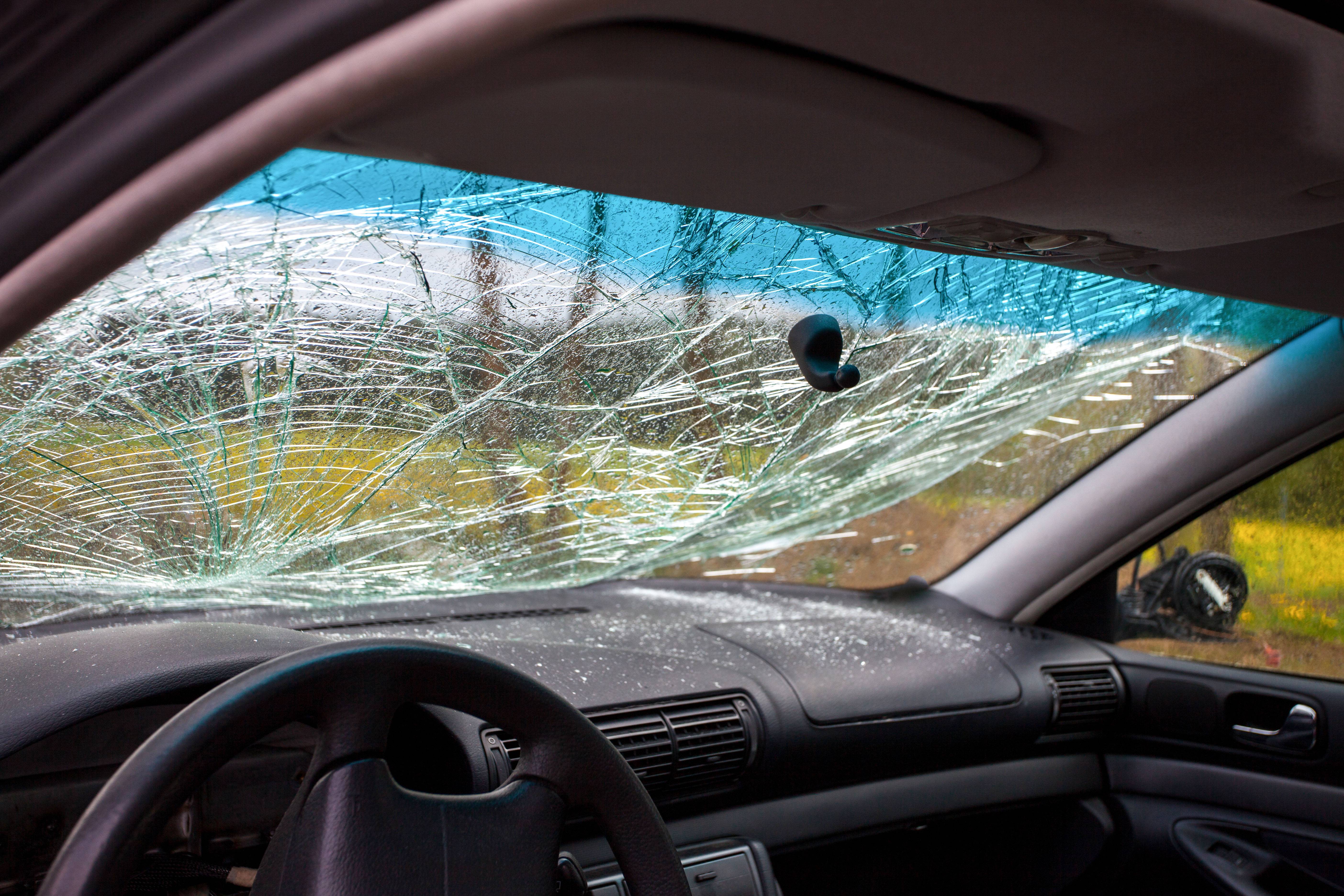 View of the interior of a wrecked car, shattered front window is seen with pieces of glass on the front desk